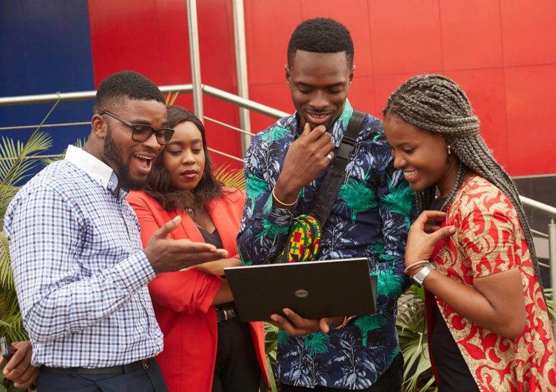 Four young adults collaborating on a project using a laptop outdoors, showcasing teamwork and diversity.